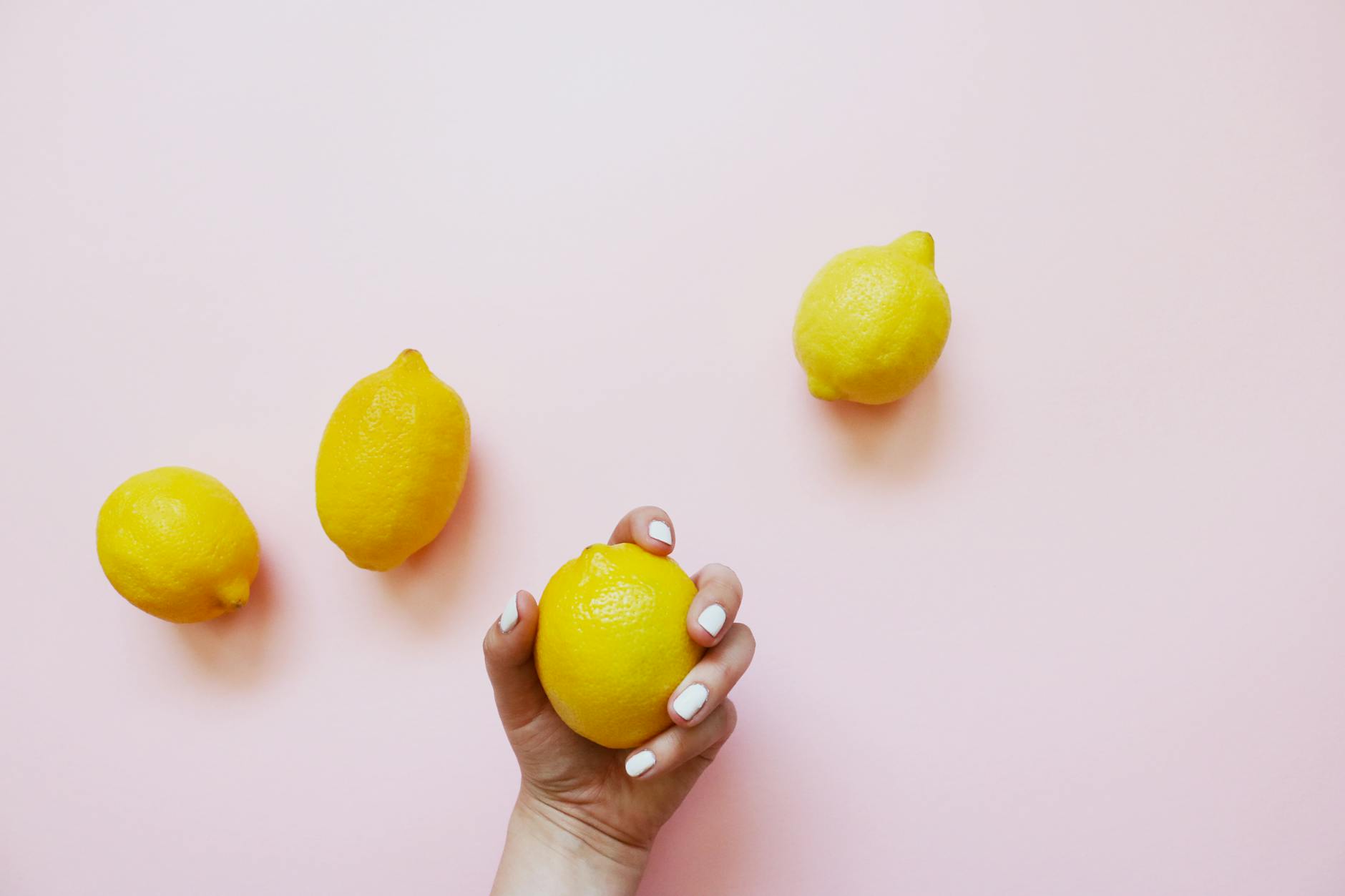 A hand holding a fresh lemon on a soft pink background, symbolizing the citrus-inspired design of Lemon Intimacy products.