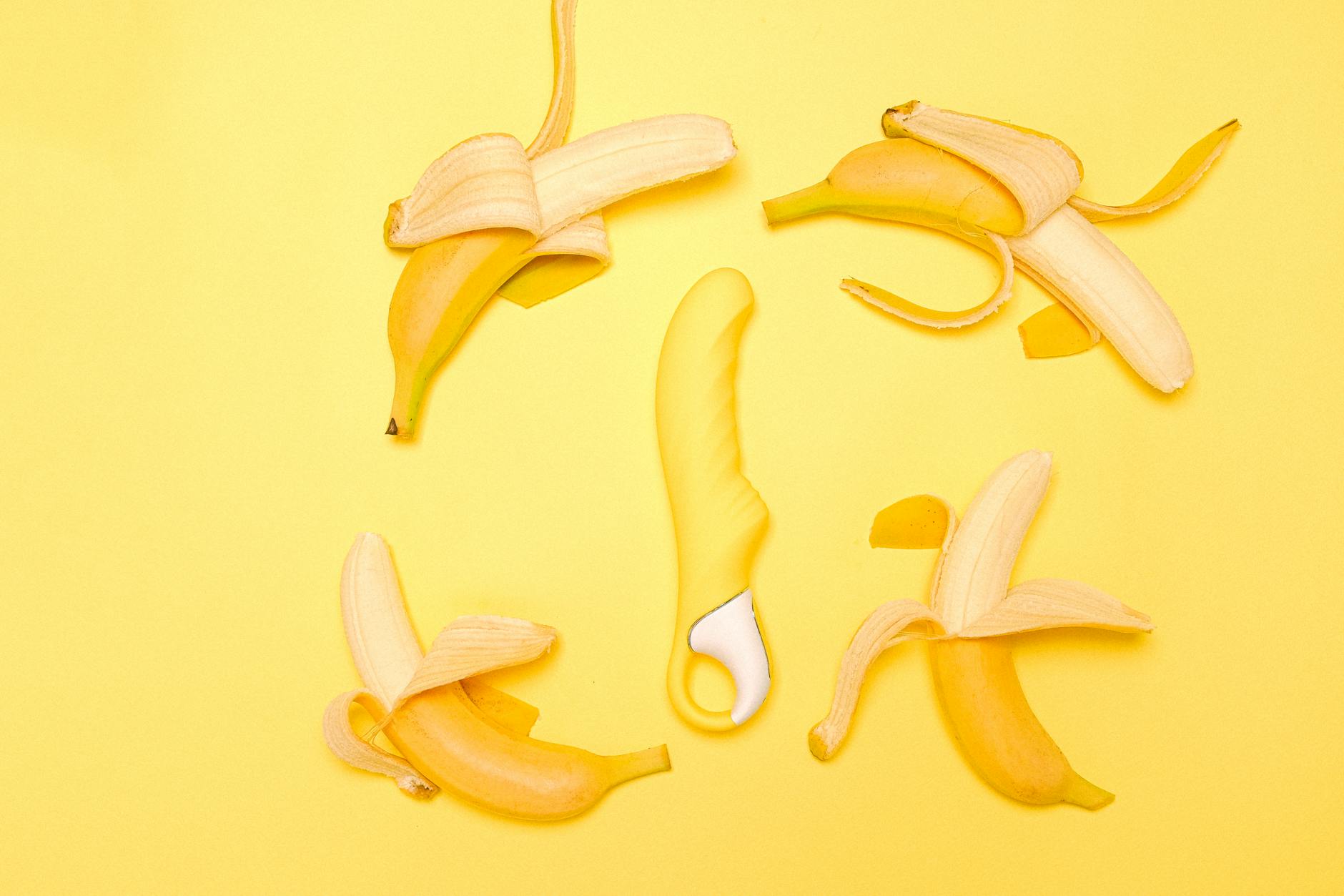 A yellow Lemon clitoral vibrator on a yellow background with fresh peeled bananas