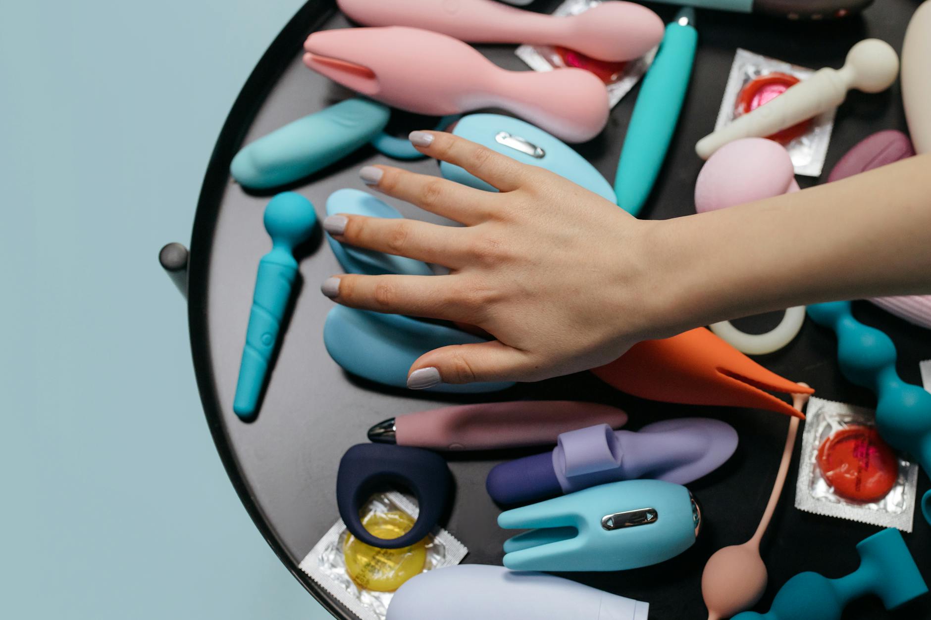 A hand reaching over a variety of colorful lemon sexual toys and vibrators arranged on a table.