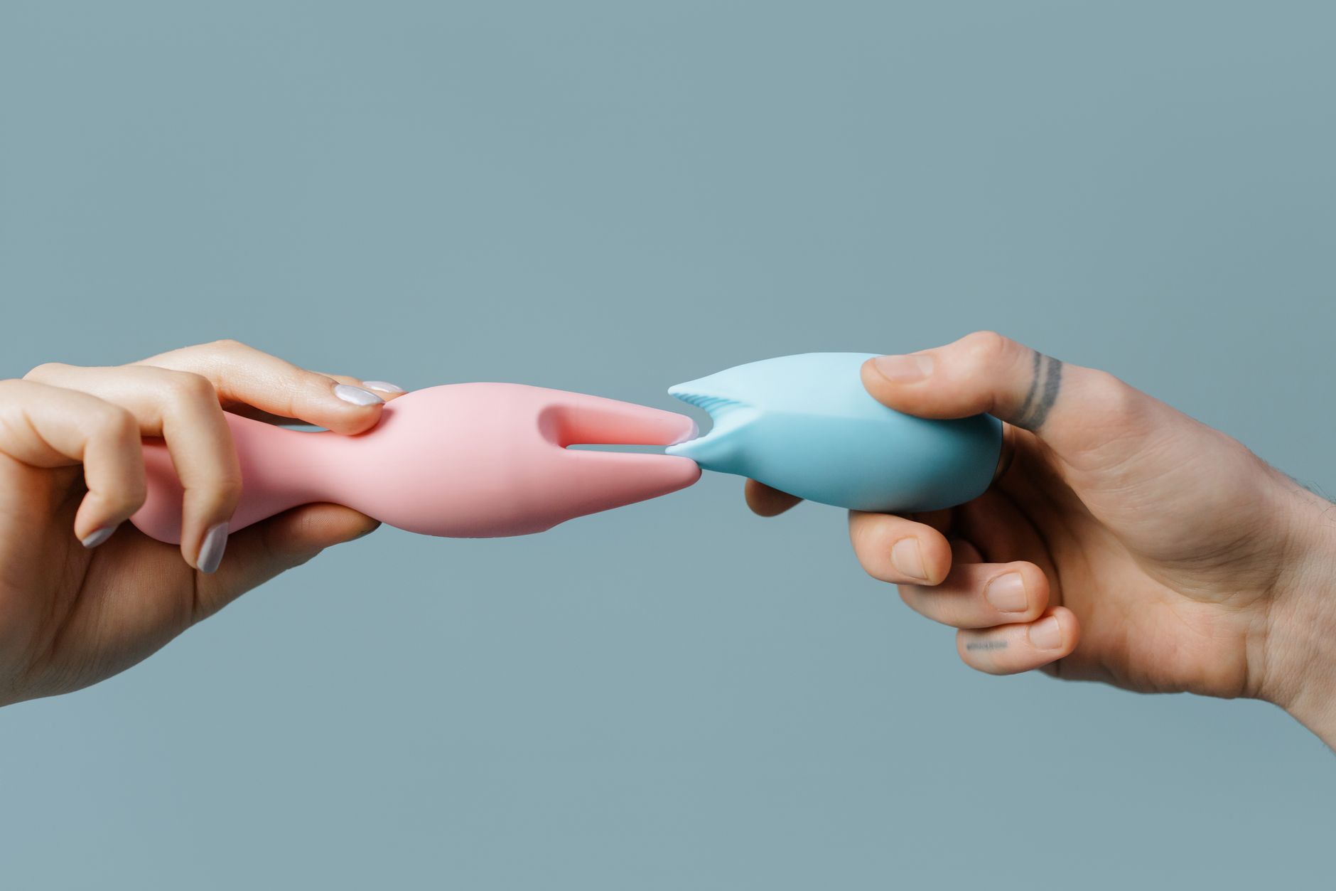 A blue silicone clitoral vibrator held in hand against a purple background