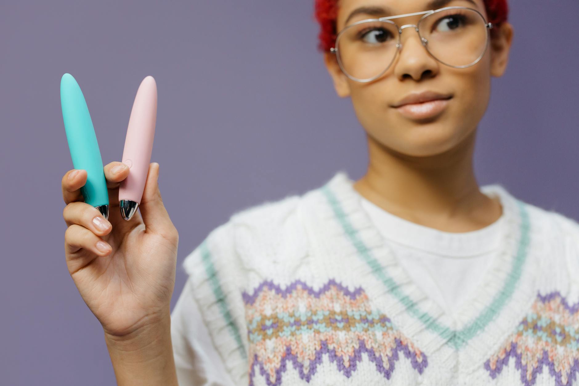 Person holding colorful vibrators against a purple background, symbolizing self-directed pleasure and empowerment