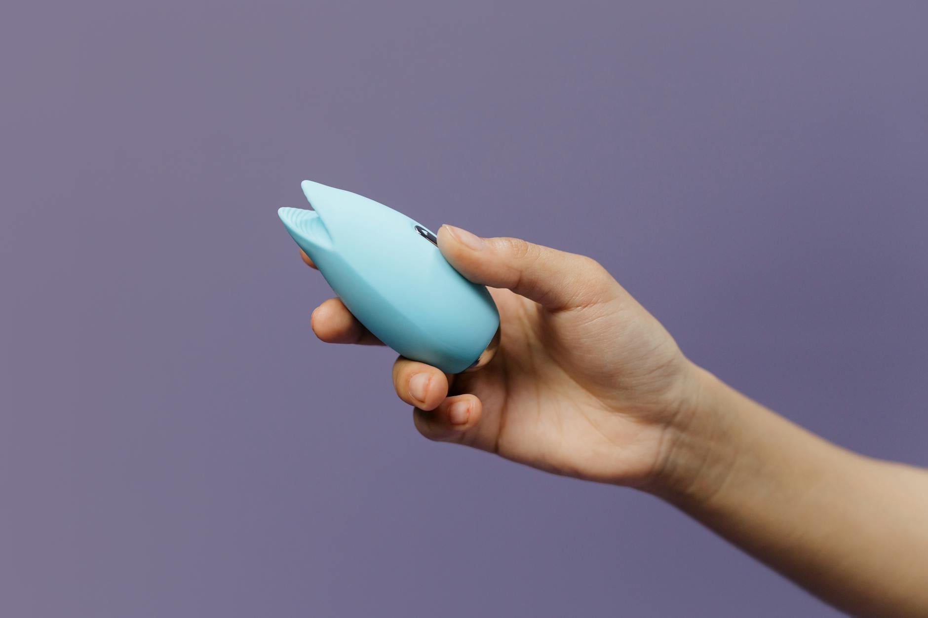 A clitoral vibrator held in hand against a purple background
